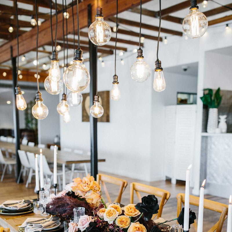 Festoon string lights with various types of globes and lengths displayed indoors in an industrial wedding with flowers.