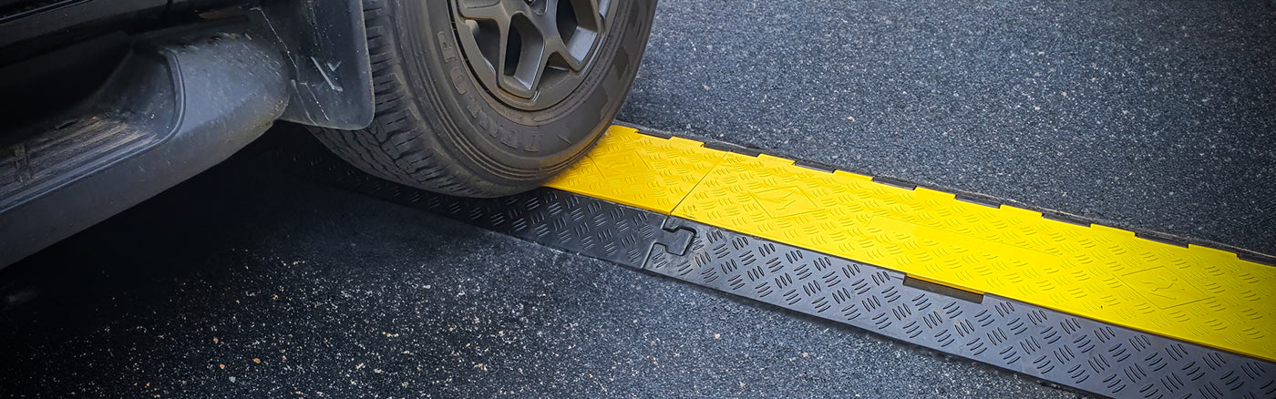 High visibility yellow and black cable guards with a car wheel driving over it.